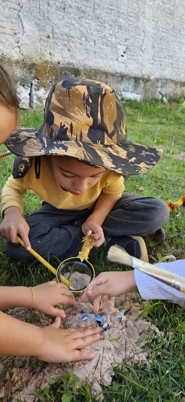 Estudante da Educação Infantil explora achados com lupa e pincel em atividade ao ar livre na Escola Lumiar Poços de Caldas